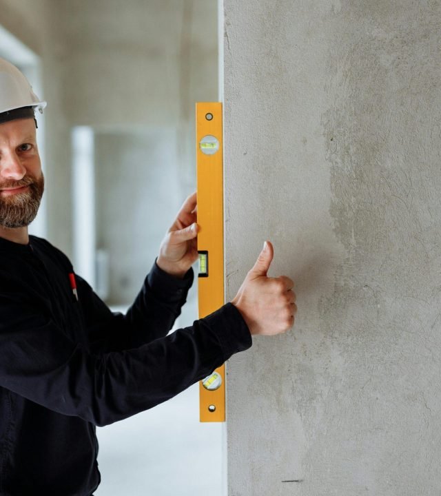 Confident male construction worker using a spirit level on a concrete wall for precise alignment indoors.